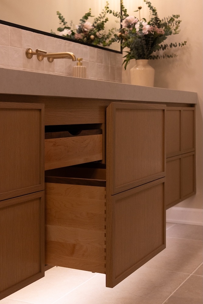 A modern bathroom vanity with open wooden drawers and a white countertop, featuring a gold faucet.