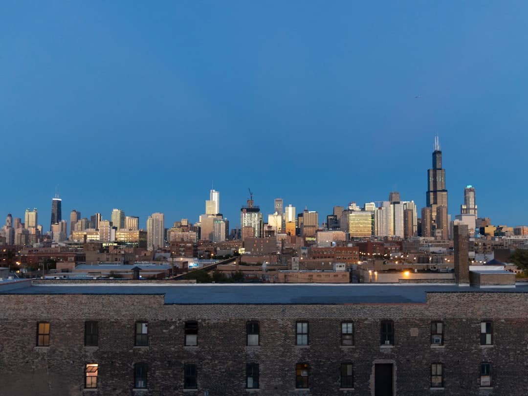 City skyline at dusk with a brick rooftop in the foreground and tall skyscrapers in the distance against a blue sky with fading light.