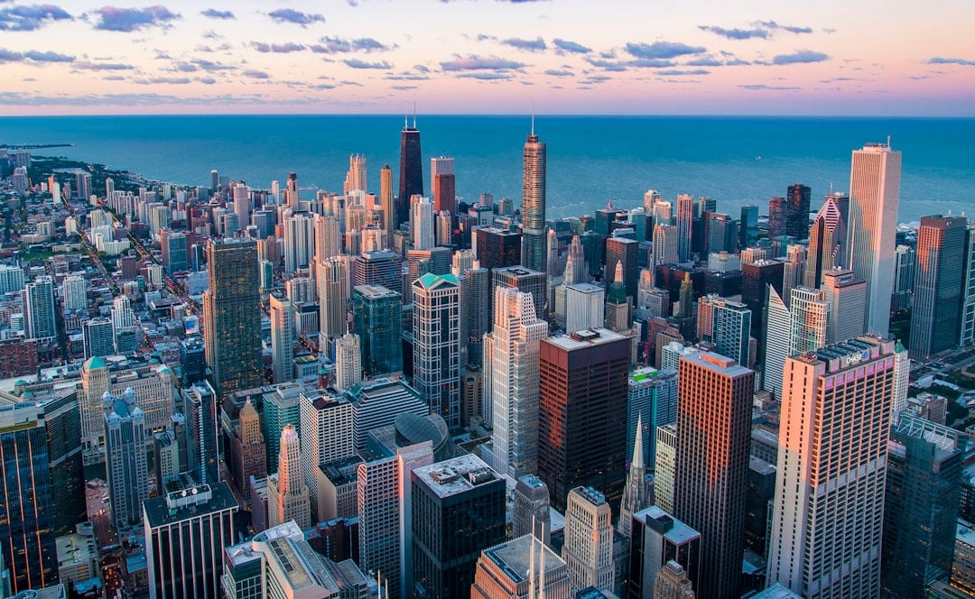 Aerial view of a dense downtown skyline along a calm lake at sunset.